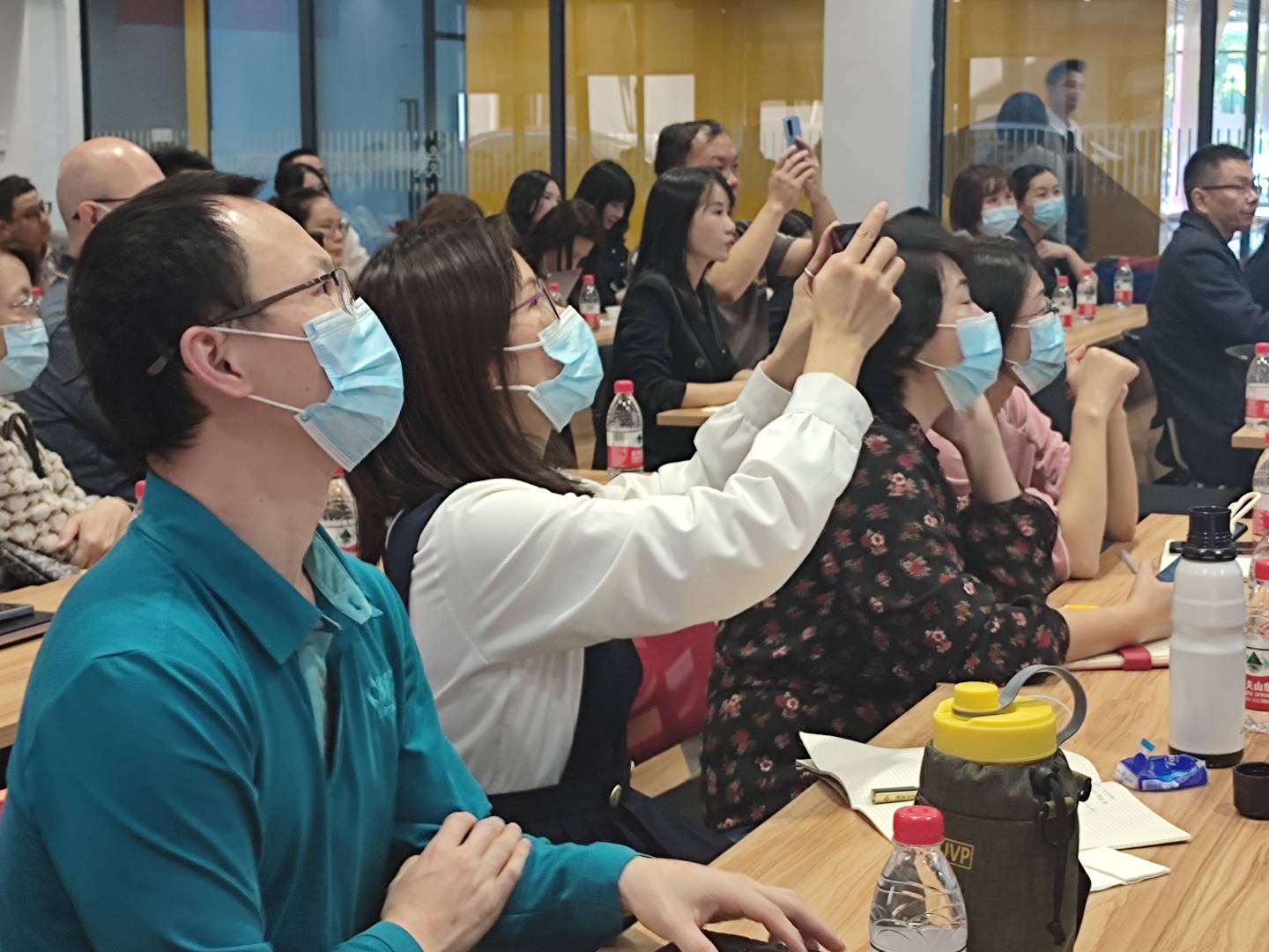 教室里的学员举手交流，桌上摆着电脑和学习笔记